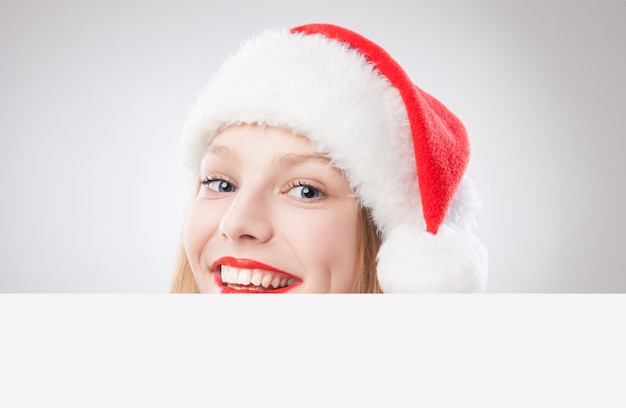 Bella donna di natale in cappello della santa che tiene scheda vuota isolata su sfondo bianco