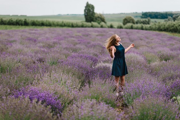 Bella donna divertente passeggiata sul campo di lavanda al tramonto Bella ragazza in abito stand e capelli lunghi volanti sul campo di lavanda viola Soft focus Godetevi la radura floreale estate natura Acconciatura