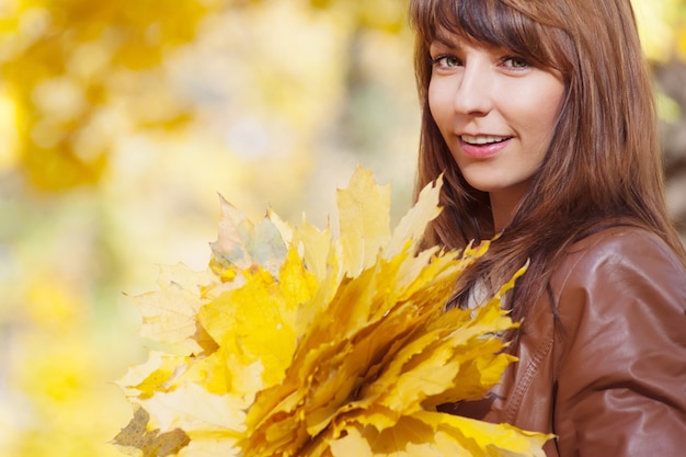 Bella donna elegante con bouquet di foglie gialle in piedi in un parco in autunno Sfondo autunnale