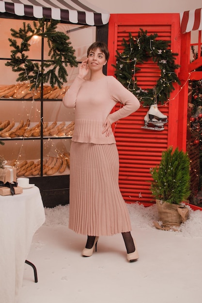 Bella donna elegante con capelli ondulati che posano in interni decorati con luci natalizie.