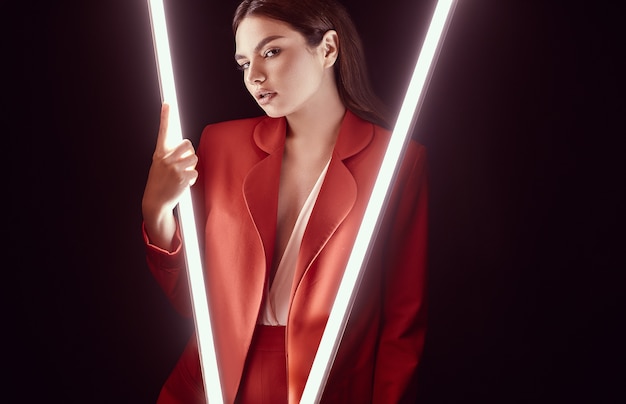 Bella donna elegante in un vestito alla moda rosso che posa con le luci al neon