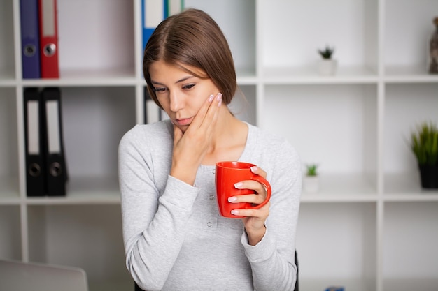 Bella donna esausta in ufficio che soffre di un forte mal di denti