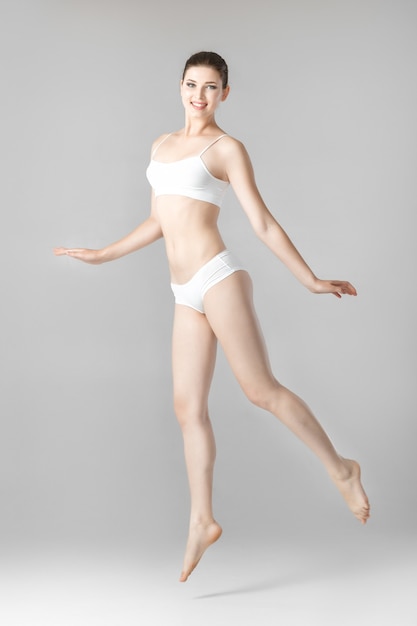 Bella donna esile con un corpo perfetto in biancheria bianca che salta su un gray