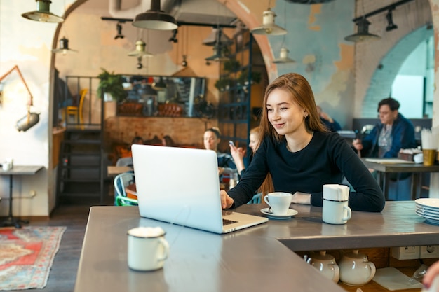 Bella donna felice che lavora al computer portatile durante la pausa caffè nella barra del caffè