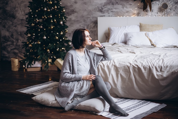 Bella donna felice che si distende sul letto vicino all'albero di Natale