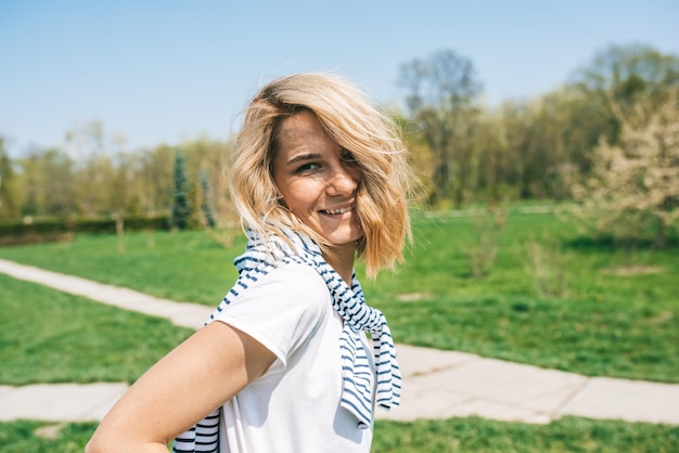 Bella donna felice con capelli biondi che soffiano sorridente e in posa sullo sfondo della natura Ritratto di giovane donna caucasica sorriso con capelli ventosi nel parco Concetto di persone e stile di vita