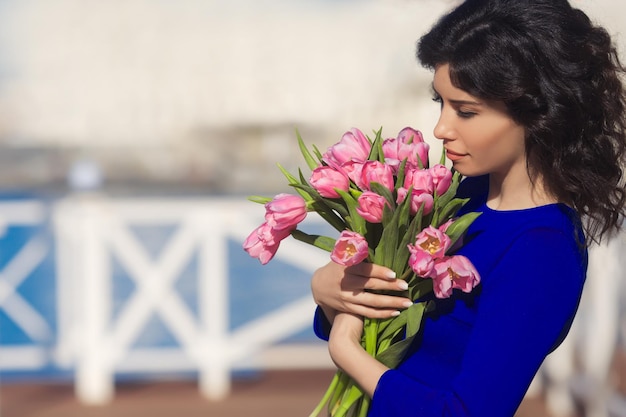 Bella donna felice con capelli castani ricci che odorano e tengono i tulipani rosa del mazzo