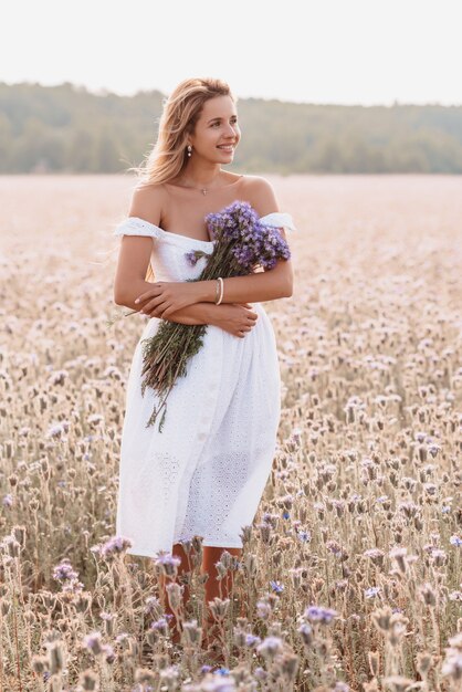 Bella donna felice in un abito bianco in un campo di fiori in estate nella natura