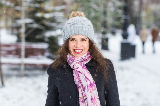 Bella donna felice vestita di cappotto nero, sciarpa rosa e cappello grigio