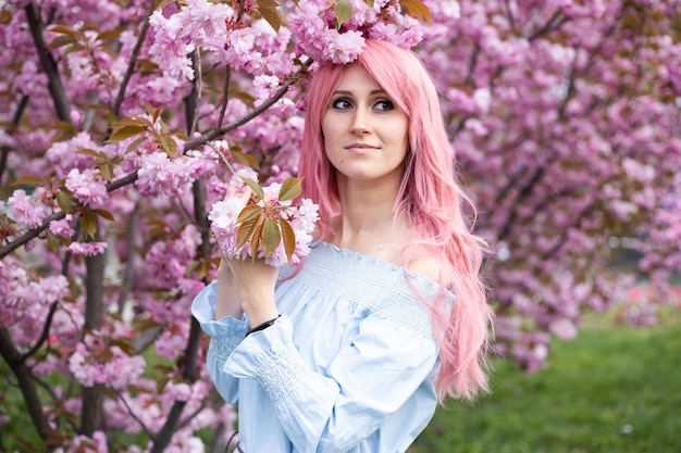 Bella donna felice vicino all'albero in fiore rosa sakura in abito blu