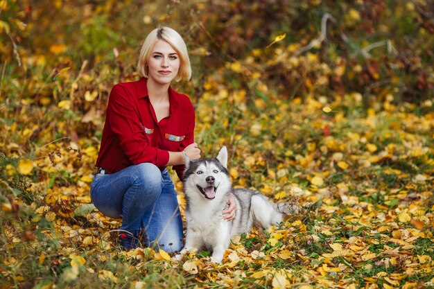 Bella donna gioca con il cane husky nella foresta di autunno