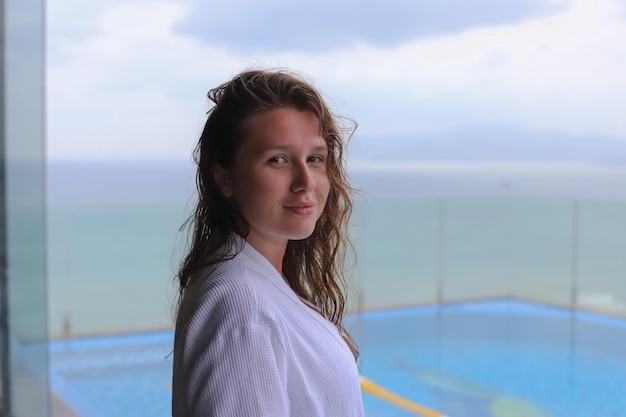 Bella donna giovane ragazza in un accappatoio bianco in un hotel di lusso spa sul tetto con vista mare o oceano le isole riposano rilassandosi e sorridendo godendosi la vacanza