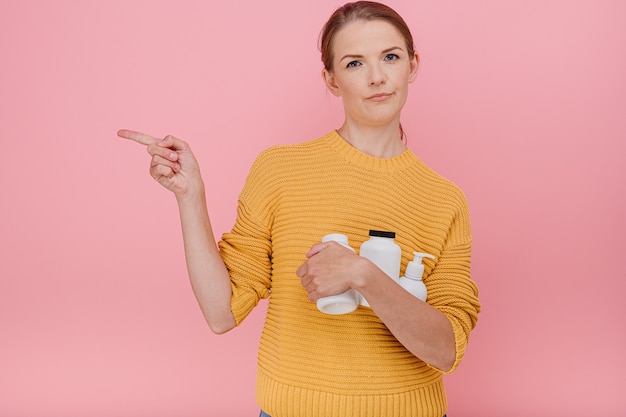 Bella donna graziosa che tiene in mano una bottiglia di pillole mediche o vitamine vestita casualmente con espressione dubbiosa