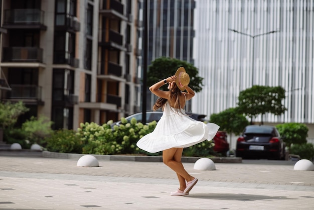 Bella donna graziosa in vestito bianco che cammina alla via della città