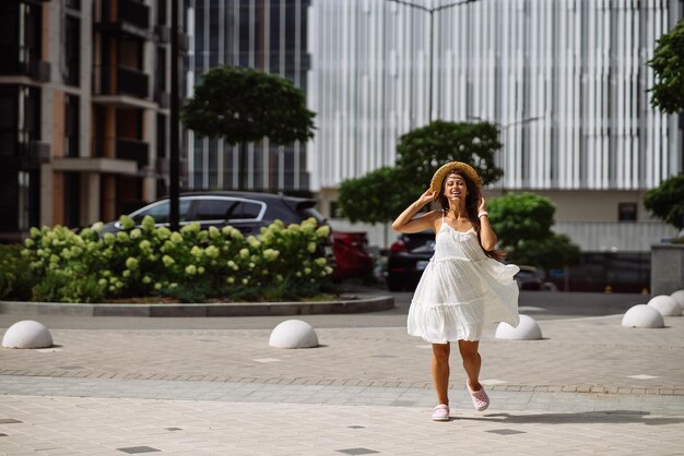 Bella donna graziosa in vestito bianco che cammina alla via della città