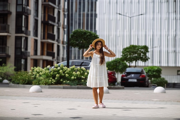 Bella donna graziosa in vestito bianco che cammina alla via della città