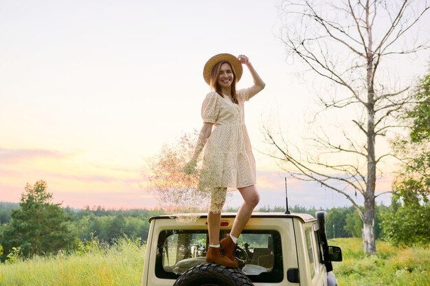 Bella donna in abito cappello di paglia con bouquet di fiori sul tetto dell'auto