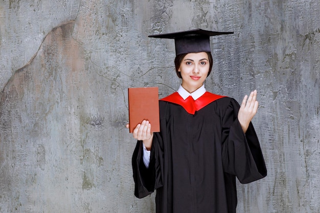 Bella donna in abito di laurea in posa con il libro. Foto di alta qualità