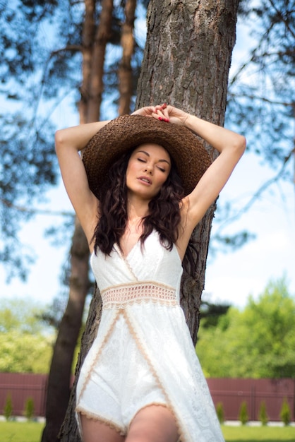 Bella donna in abito estivo bianco e cappello di paglia in giardino