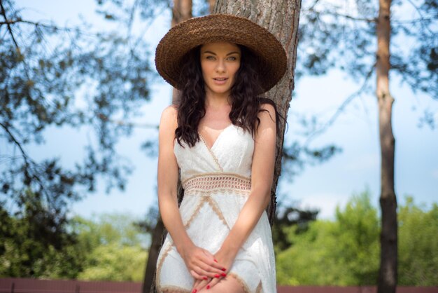 Bella donna in abito estivo bianco e cappello di paglia in giardino