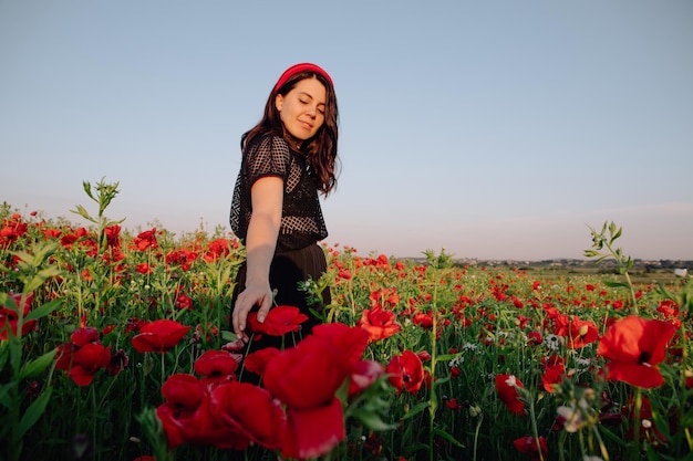 Bella donna in abito nero sul tramonto al campo di fiori di papaveri