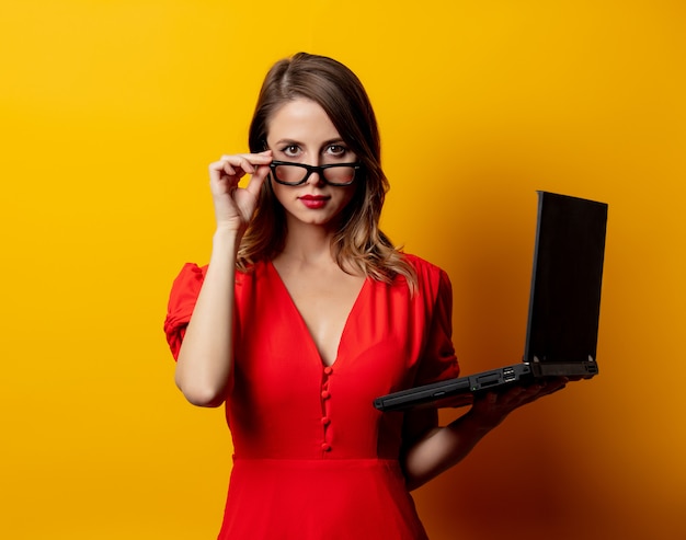 Bella donna in abito rosso con computer portatile sul muro giallo