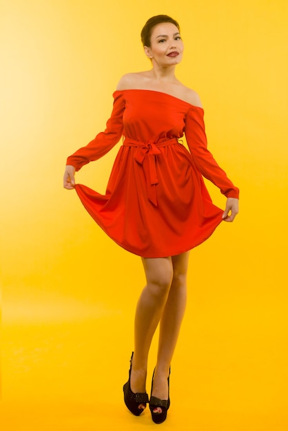 Bella donna in abito rosso in posa su sfondo giallo