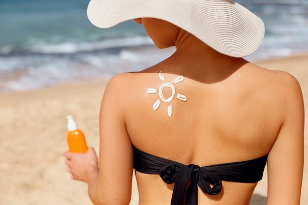 Bella donna in bikini che applica crema solare sulla spalla abbronzata.