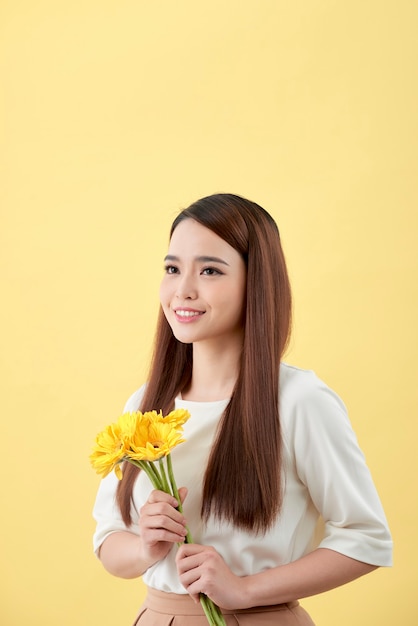 Bella donna in camicia bianca con fiori gerbera in mano su uno sfondo giallo. Lei sorride e ride