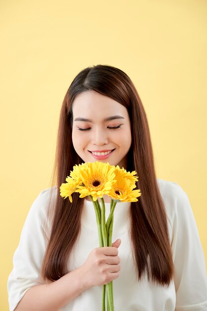 Bella donna in camicia bianca con fiori gerbera in mano su uno sfondo giallo. Lei sorride e ride