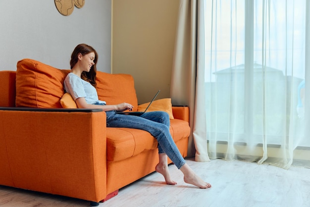 Bella donna in chat sul divano arancione con un laptop Stile di vita