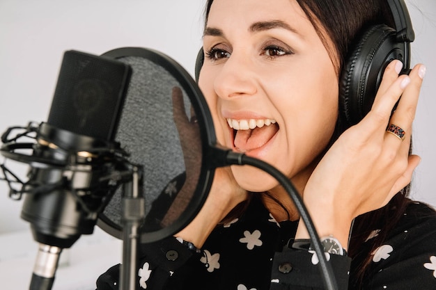 Bella donna in cuffia canta una canzone vicino a un microfono in uno studio di registrazione