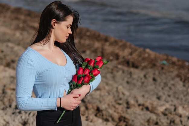 Bella donna in maglietta blu e pantaloni neri tiene un mazzo di rose rosse all'aperto il giorno di San Valentino