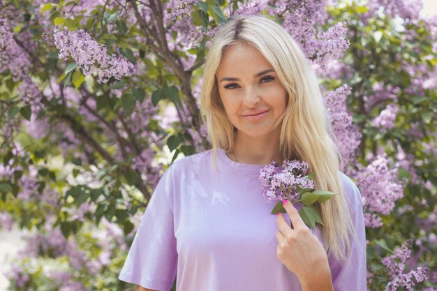 Bella donna in maglietta viola tra i cespugli di lillà in fiore in una giornata di primavera