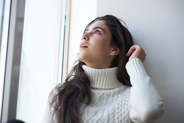 Bella donna in maglione bianco vicino alla finestra