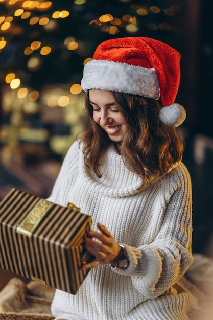 Bella donna in maglione caldo, calzini e cappello di Natale, seduta sul pavimento