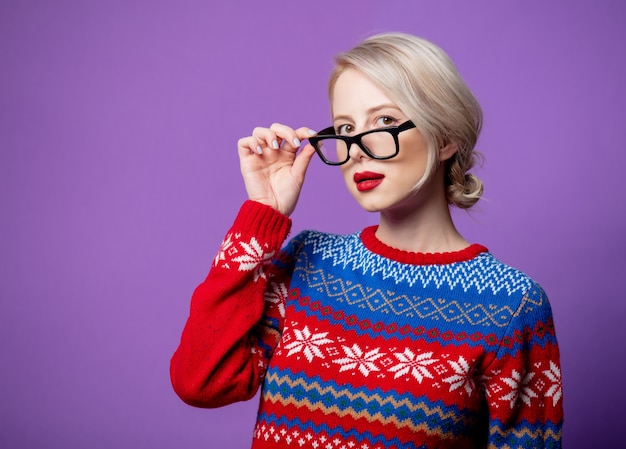 Bella donna in maglione di Natale e bicchieri su sfondo viola