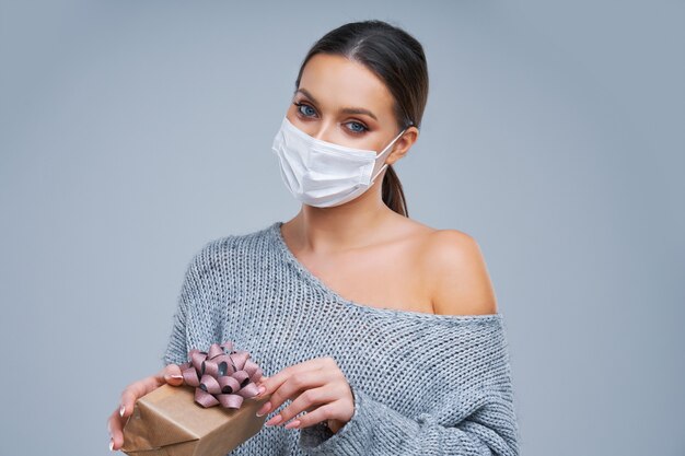 bella donna in maschera che tiene presente su sfondo grigio