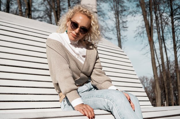 Bella donna in occhiali da sole sulla panchina in autunno parco da solo, concetto di stile di vita della gente