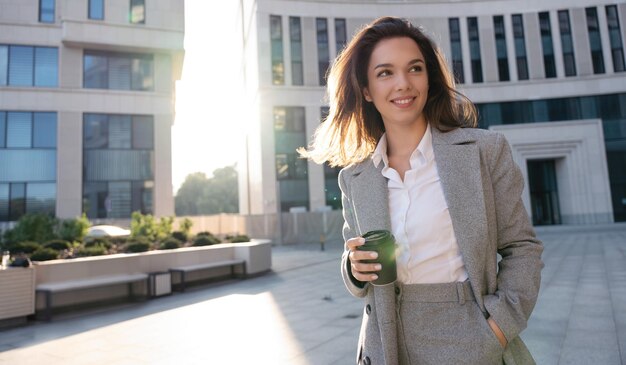 Bella donna in piedi con caffè vicino edificio per uffici Ritratto di donna di successo che tiene tazza di bevanda calda