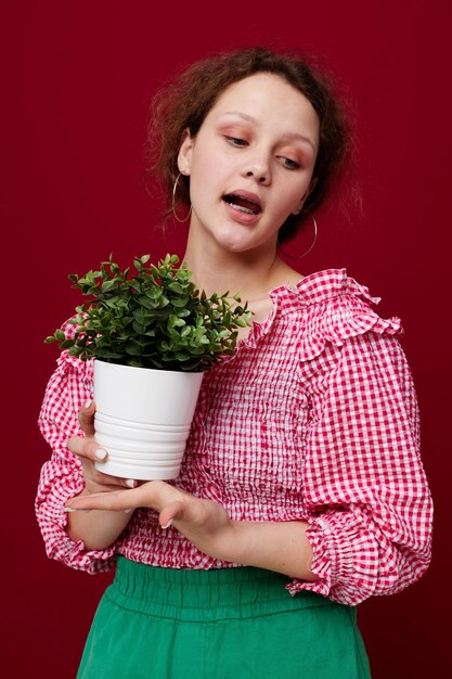 Bella donna in piedi e tenendo il fiore in vaso sfondo rosso inalterato