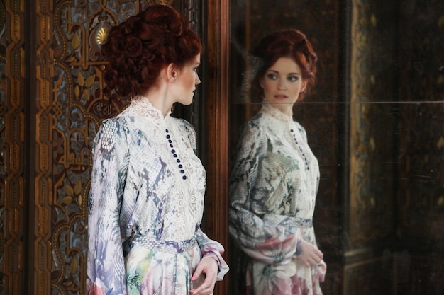 Bella donna in piedi nella stanza del palazzo con lo specchio