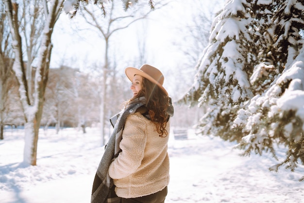 Bella donna in piedi tra alberi innevati e godendo la prima neve. Tempo felice. Natale.