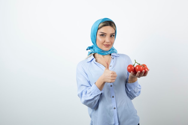 Bella donna in scialle che mostra il pollice in su e che tiene i pomodori rossi