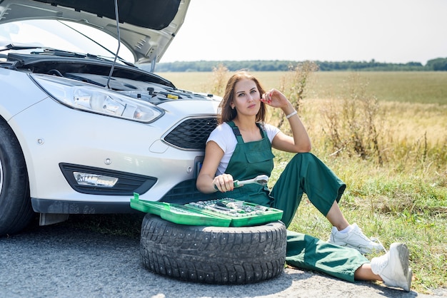 Bella donna in tuta con le chiavi che ripara un'auto rotta nel suo viaggio