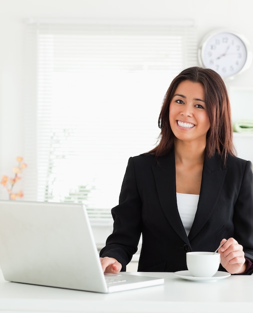 Bella donna in tuta godendo una tazza di caffè mentre vi rilassate con il suo computer portatile