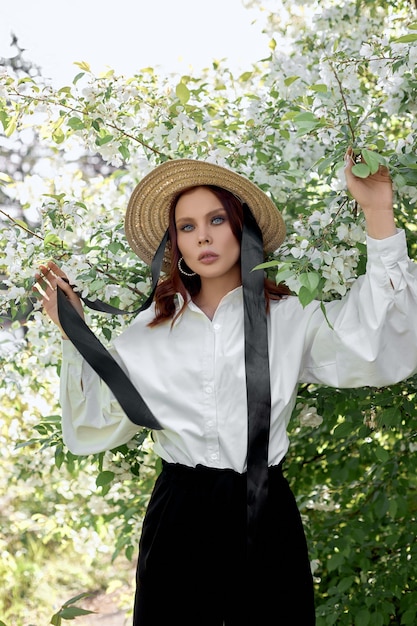 Bella donna in un cappello in primavera tra i rami dei cespugli di mele in fiore