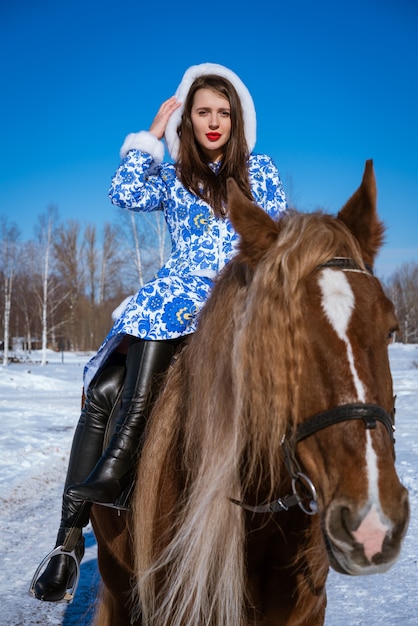 Bella donna in un cappotto blu a cavallo in inverno in una giornata di sole