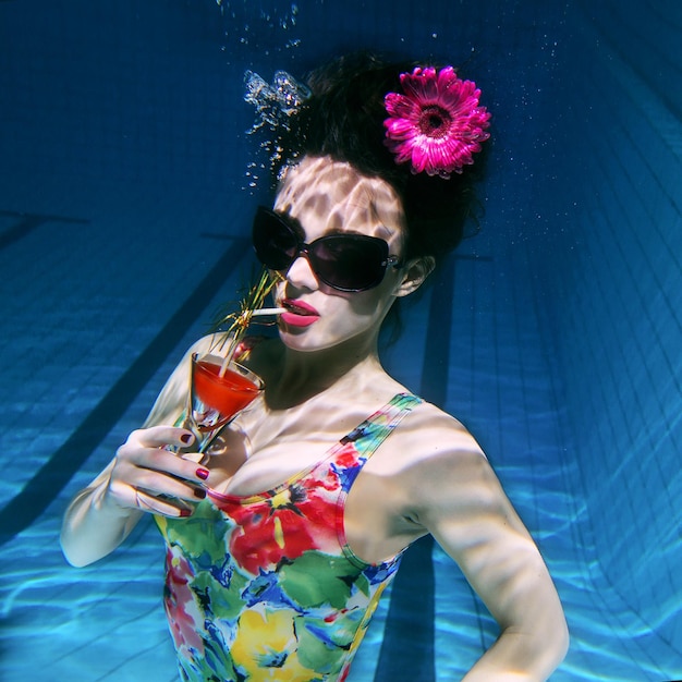 bella donna in un costume da bagno alla moda colorato e occhiali da sole e gerbera rosa in testa con