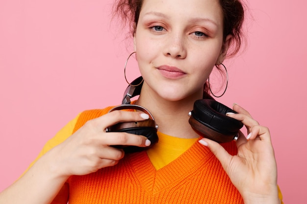 Bella donna in un maglione arancione cuffie musica intrattenimento sfondo rosa inalterato